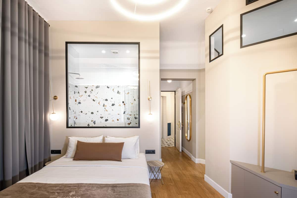 A modern bedroom with a large bed, a mirror, and a view of a bathroom.