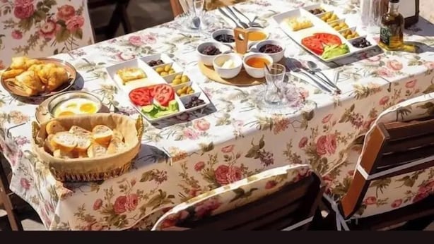 Ulkoterassi, jossa on ruokapöytiä, kukalliset pöytäliinat, kiviseinät sekä tarjolla erilaisia ruokia ja juomia.