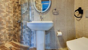 Kylpyhuone, jossa on lasiseinällä varustettu suihku, valkoinen pesuallas ja sen yläpuolella peili sekä wc-istuin.