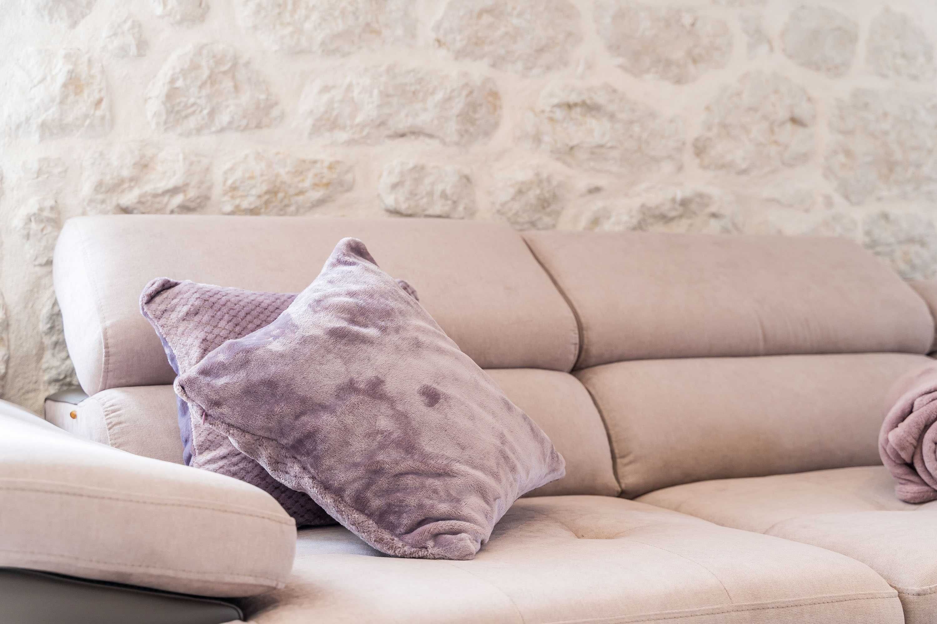A beige sofa with two pillows, a stone wall background, and a small table with a cushion.