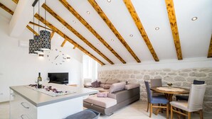 A modern loft with exposed wooden beams, a stone wall, a sofa, and a dining area with chairs. - Villa Ro-ma (Dubrovacko Primorje)