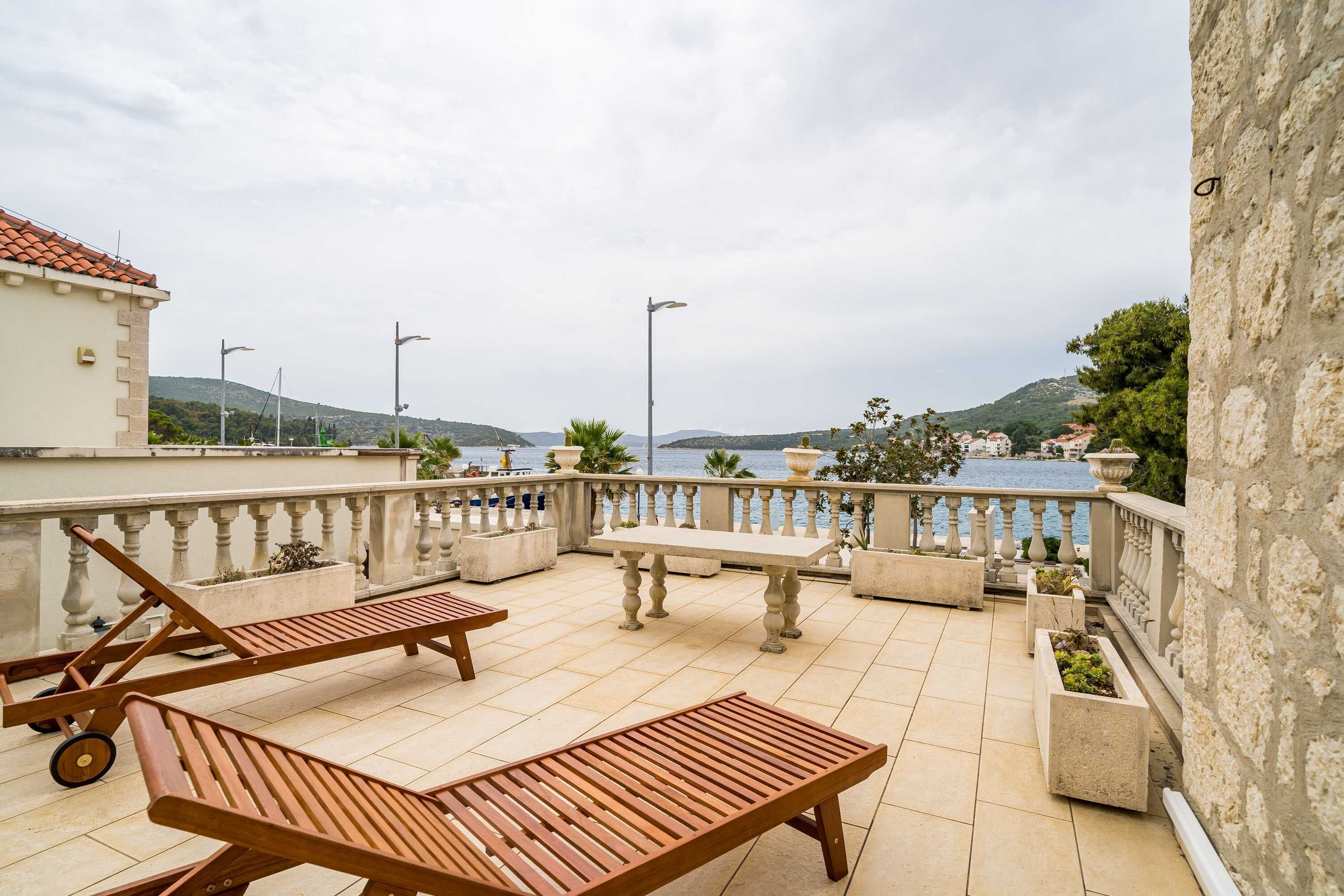 A terrace with lounge chairs and a table, overlooking a body of water and hills.