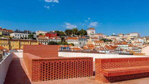 A rooftop terrace with red brick walls and a view of a cityscape with various buildings.