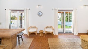 A spacious room with a wooden ceiling, two wicker chairs, a wooden table, and a woven rug. - Amazing Comporta family beach house (Comporta)