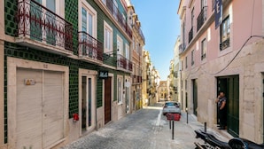 A narrow cobblestone street lined with colorful buildings, a motorcycle parked on the right, and a car parked on the left.