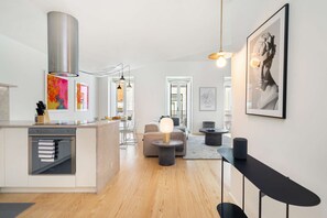 Eine moderne Küche mit Kochinsel, ein Essbereich mit rundem Tisch und ein Wohnbereich mit Sofa und Couchtisch.