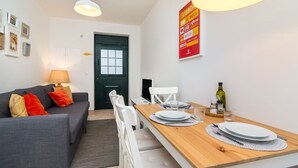 A modern living room with a grey sofa, white chairs, a wooden dining table, and a black door.