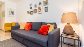 A modern living room with a grey sofa, colorful cushions, a yellow armchair, and a table with a lamp.