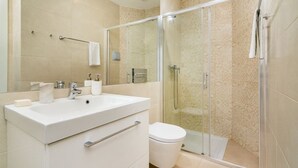 A modern bathroom with a glass-enclosed shower, a white sink, and a toilet.