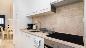 A modern kitchen with white cabinets, a black stovetop, and a marble backsplash.