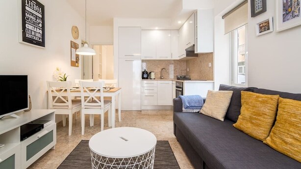 Een moderne woonkamer met een grijze bank, een eettafel en een keukenhoek.