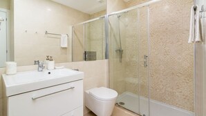 Een moderne badkamer met een douchecabine van glas, een witte wastafel en een toilet.