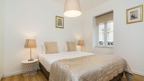 Een slaapkamer met een bed, twee bedlampjes, een hangende lamp, een raam en een foto aan de muur.