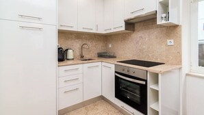 Een kleine keuken met witte kasten, een zwarte oven en een aanrecht met waterkoker en koffiezetapparaat.