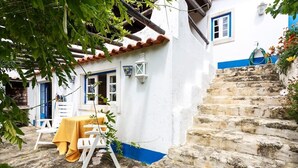 Un edificio blanco con detalles azules, una escalera de piedra y una mesa con mantel amarillo.