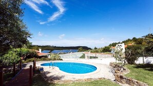 Una piscina con cubierta de madera, rodeada de césped y árboles.