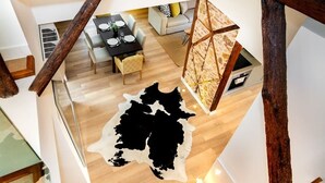 A spacious room with a large black and white cowhide rug, wooden beams, and a dining area with a table set for four. - Downtown Luxury Duplex | AC | Elevator | Wi-Fi (Lisboa)