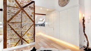 A modern kitchen with white cabinets, a stone accent wall, and a wooden beam structure. - Downtown Luxury Duplex | AC | Elevator | Wi-Fi (Lisboa)
