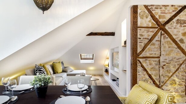 A dining area with a dark wooden table set for four, a potted plant, and a stone wall with a wooden cross beam design. - Downtown Luxury Duplex | AC | Elevator | Wi-Fi (Lisboa)