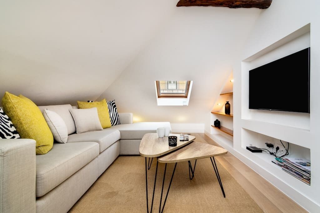 Un salon moderne avec un canapé, une table basse, un téléviseur fixé au mur et une fenêtre donnant sur un beau paysage.