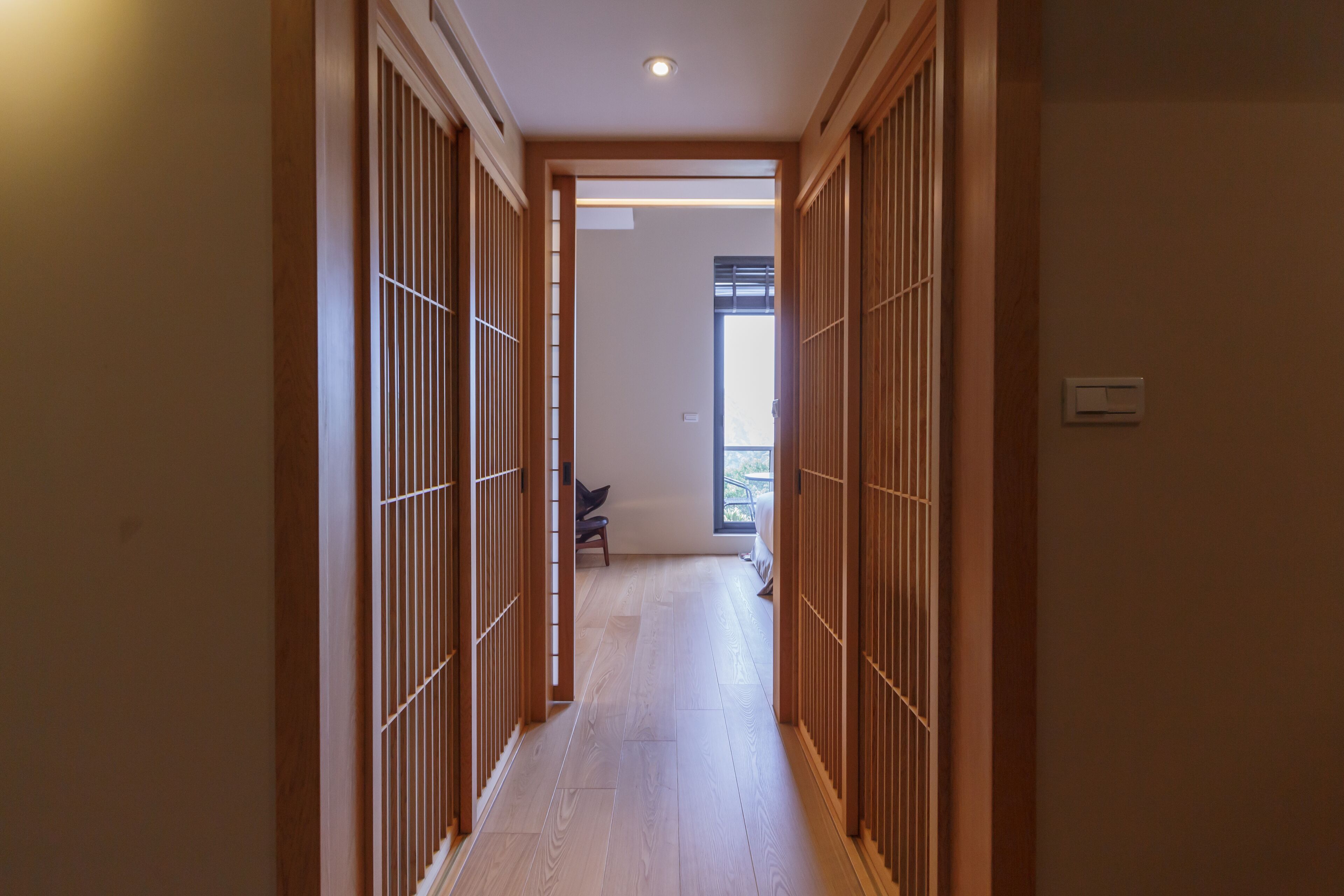 A hallway with wooden sliding doors, a bench, and a window at the end.