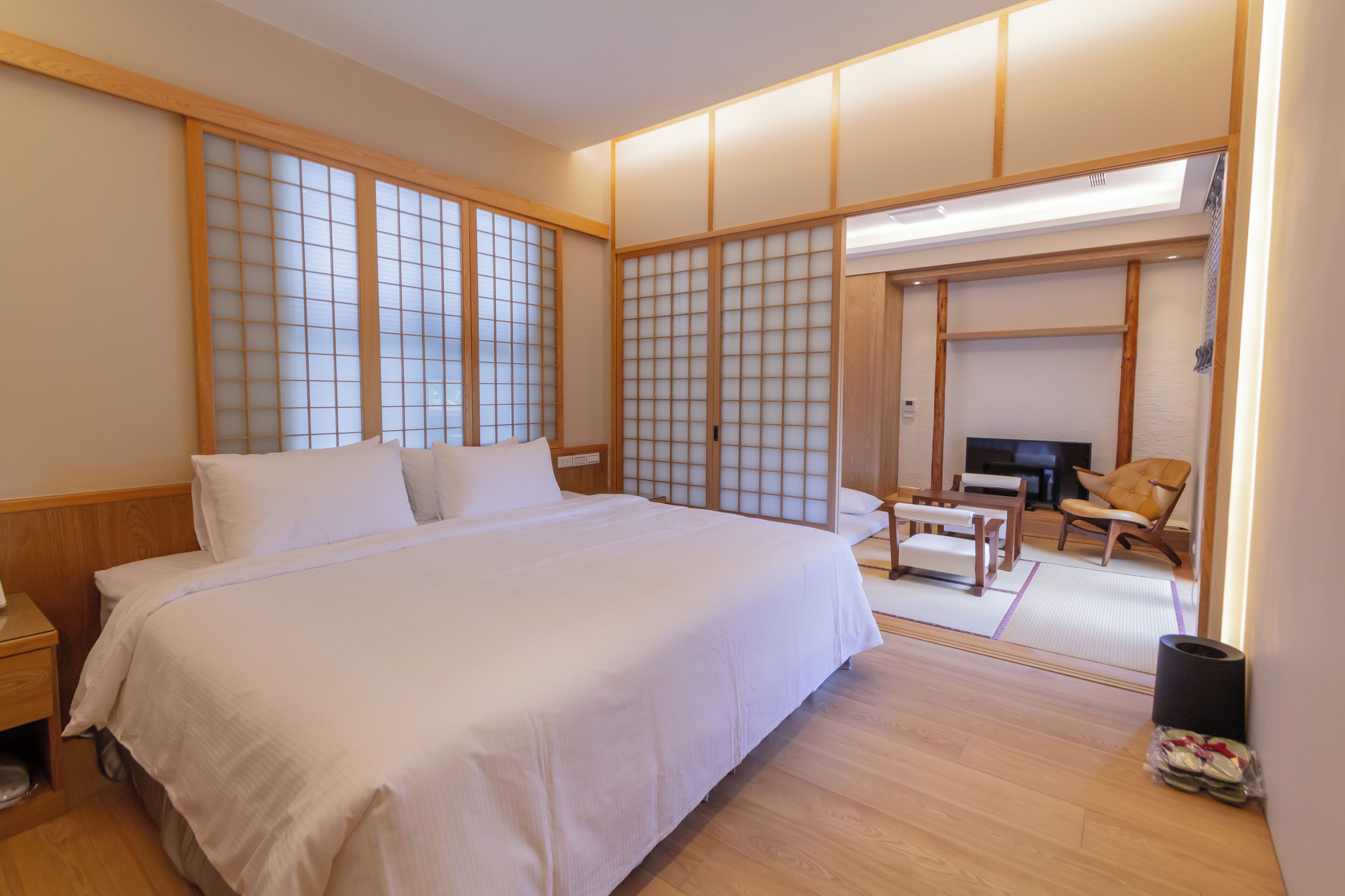 A traditional Japanese-style bedroom with tatami flooring, a large bed, a desk, and a chair.