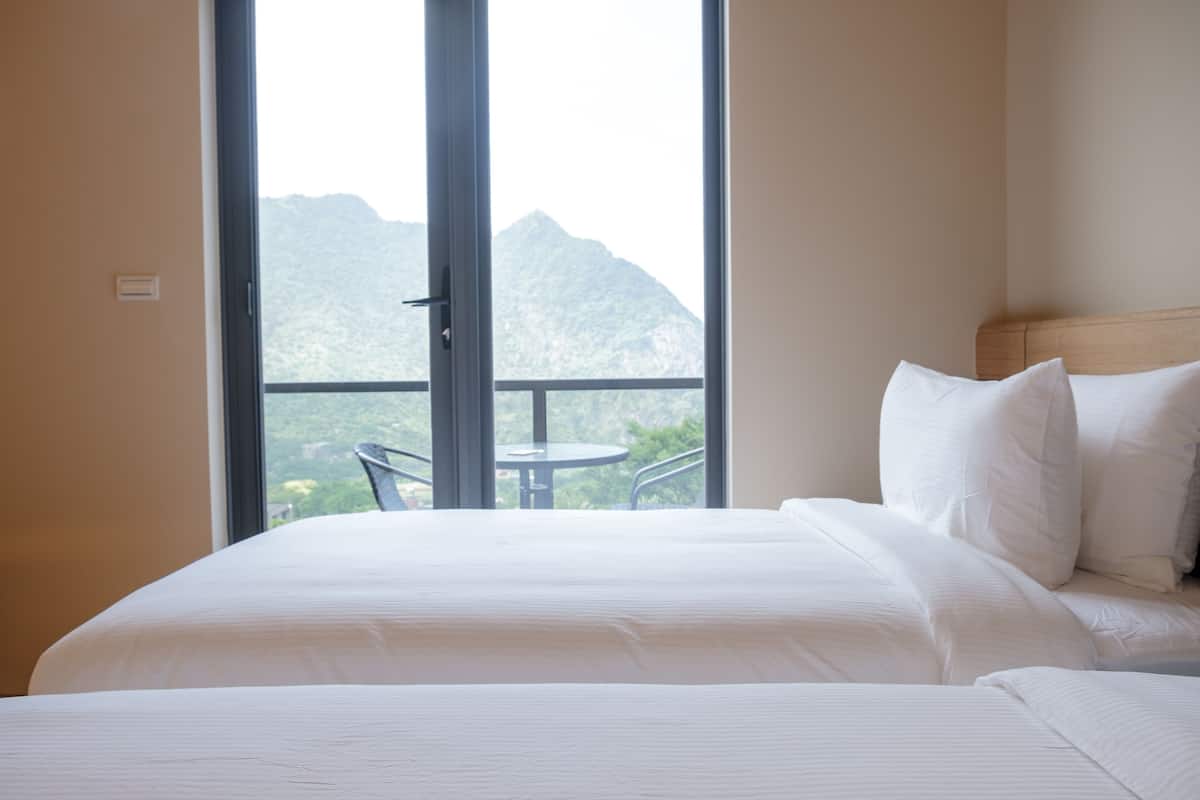 A hotel room with a large bed, white bedding, and a view of mountains through a balcony door.