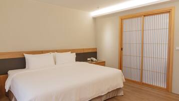 A neatly made bed with a wooden headboard, a bedside table with a telephone, and a sliding shoji screen door.