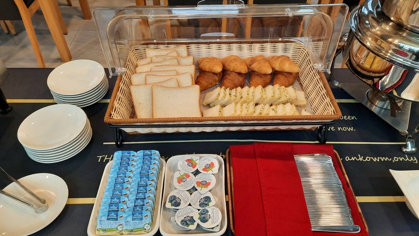 A buffet setup with bread, croissants, and cheese. There are also trays of yogurt and a red napkin holder.