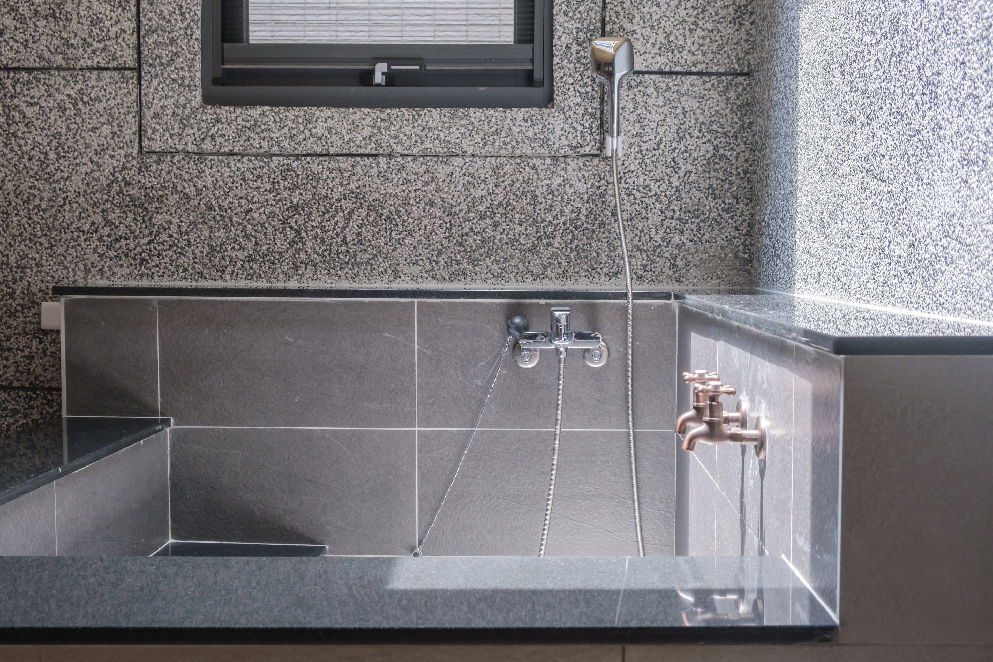 Une salle de bain moderne avec une baignoire rectangulaire, deux robinets et une fenêtre située au-dessus de la baignoire.