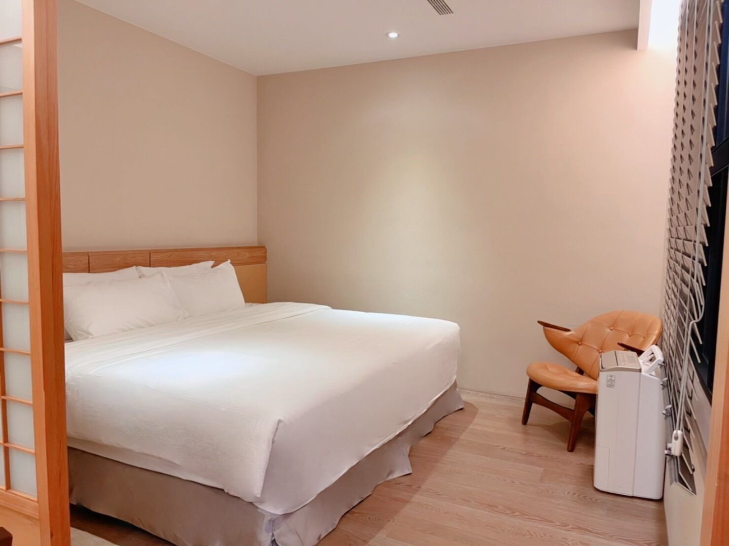 Une chambre à coucher avec un lit, une chaise et un petit appareil blanc, probablement un radiateur ou un climatiseur.