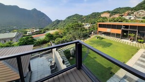 Un balcone con vista su un paesaggio montuoso, un edificio moderno e un prato curato.