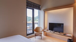 Una moderna camera d'albergo con una grande finestra, una televisione a schermo piatto, una poltrona comoda e un letto rifatto con cura.