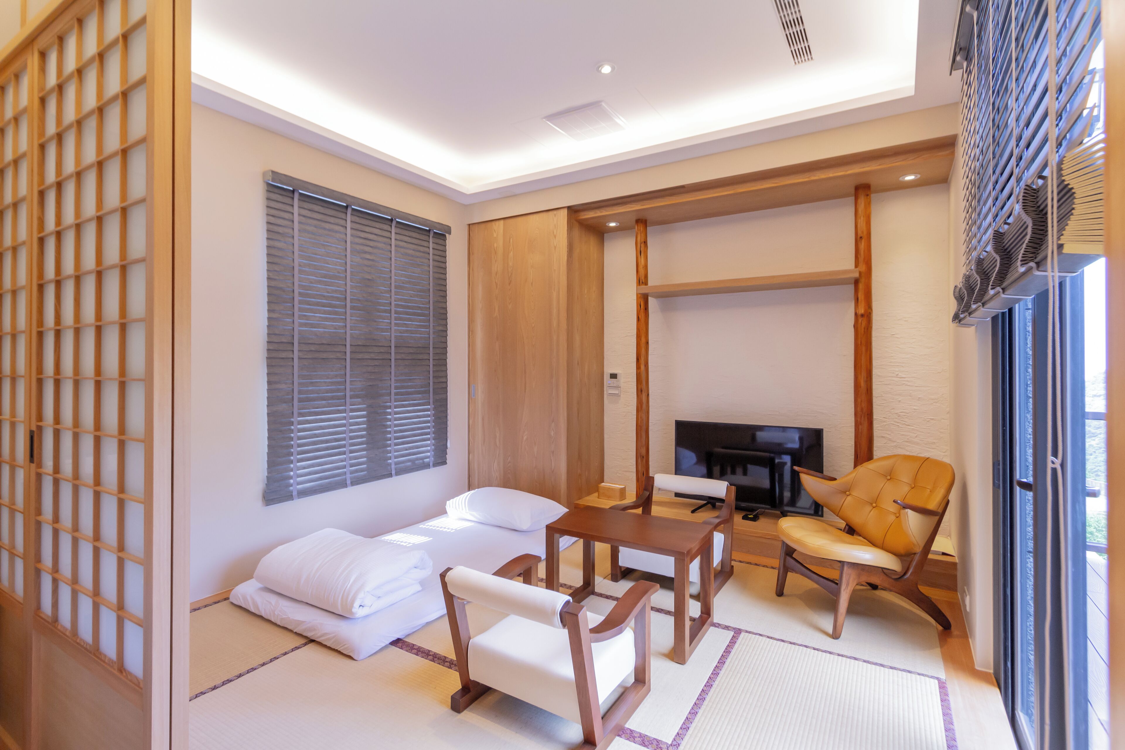 Une pièce de style japonais traditionnel, avec un sol recouvert de tatamis, une table basse, des chaises et un téléviseur.