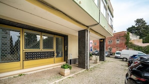 A building with a yellow facade, large windows with metal grilles, and a paved entrance area with potted plants. - Borja111 | Amazing View | AC | Elevator | Families (Lisboa)