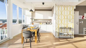 A modern kitchen with white cabinets, a dining area with a wooden table and chairs, and a view of the city through large windows. - Borja111 | Amazing View | AC | Elevator | Families (Lisboa)
