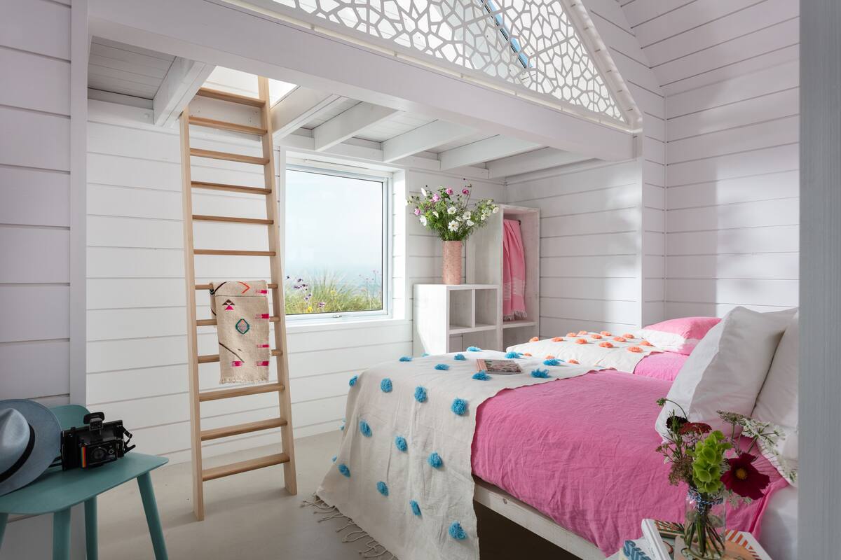 A bedroom with a bed, a ladder, a chair, a desk, and a window.