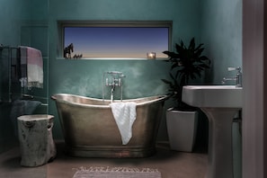 A bathroom with a freestanding bathtub, a sink, a mirror, a window with a view, and a potted plant. - Three Mile Beach (Hayle)