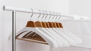 A white metal rod with wooden hangers and white garments hanging on it.