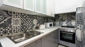 A kitchen with patterned backsplash tiles, a stainless steel sink, a microwave, and an oven.