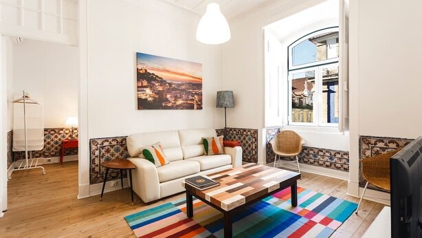 A modern living room with a white sofa, a colorful striped rug, a wooden coffee table, and a cityscape painting on the wall.
