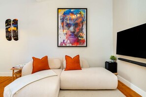 Un salon moderne avec un canapé d’angle, un tableau abstrait encadré et un téléviseur à écran plat fixé au mur.