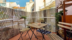 Een klein terras buiten met een houten tafel en bankjes, omgeven door een lattenhek.