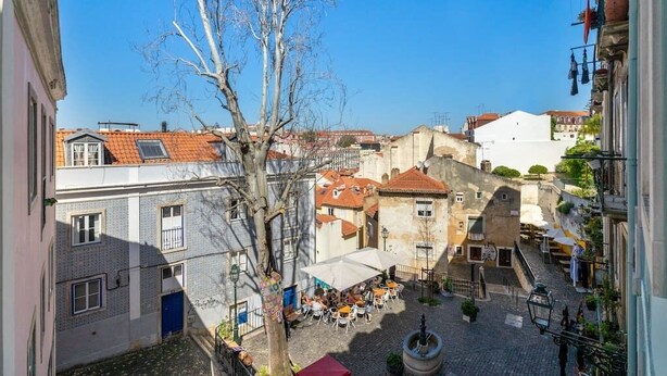 A cobblestone street with buildings, a tree, and outdoor seating for cafes.