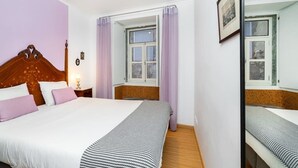 A bedroom with a wooden bed, a window with curtains, a mirror, and a small bedside table.