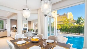 A dining area with a pool view, featuring a table set for four with plates, glasses, and a bowl of fruit.