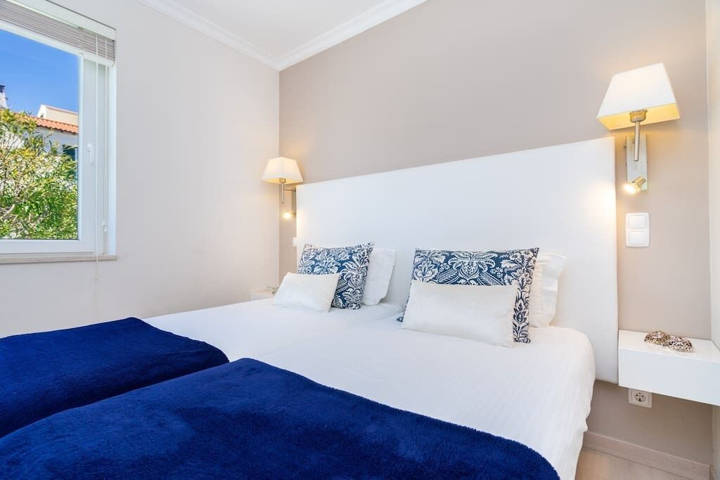 Camera d'albergo con un letto, due abat-jour e una finestra vista verde.