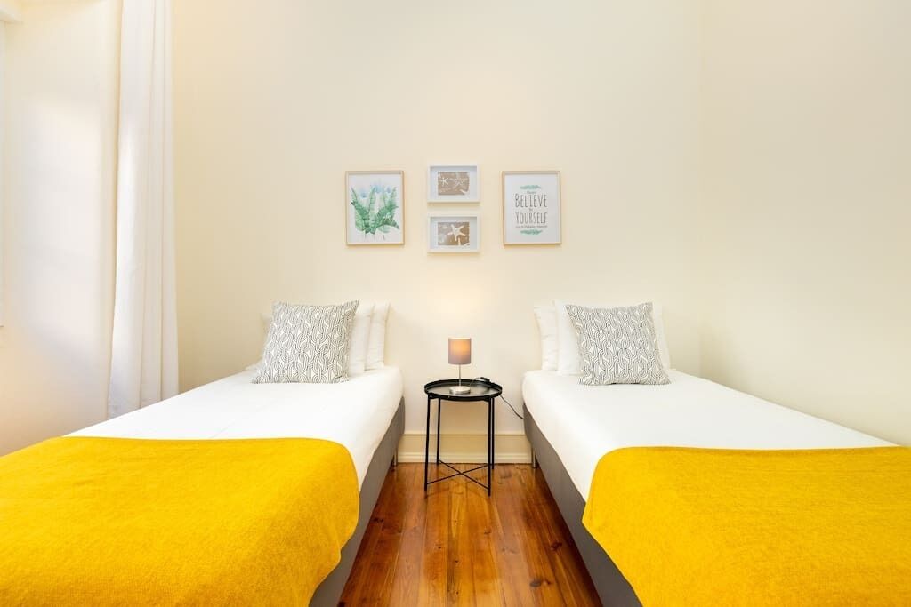 Une chambre d’hôtel avec deux lits simples, une petite table avec une lampe et trois tableaux encadrés accrochés au mur.