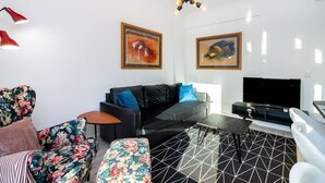 Una sala de estar moderna con un sofá negro, sillones estampados, un televisor y obras de arte en las paredes.