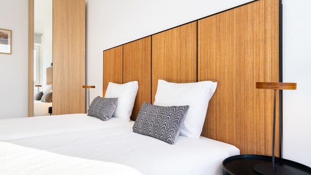 Una habitación de hotel moderna con una cama grande, cabecero de madera y una mesita de noche redonda y negra.